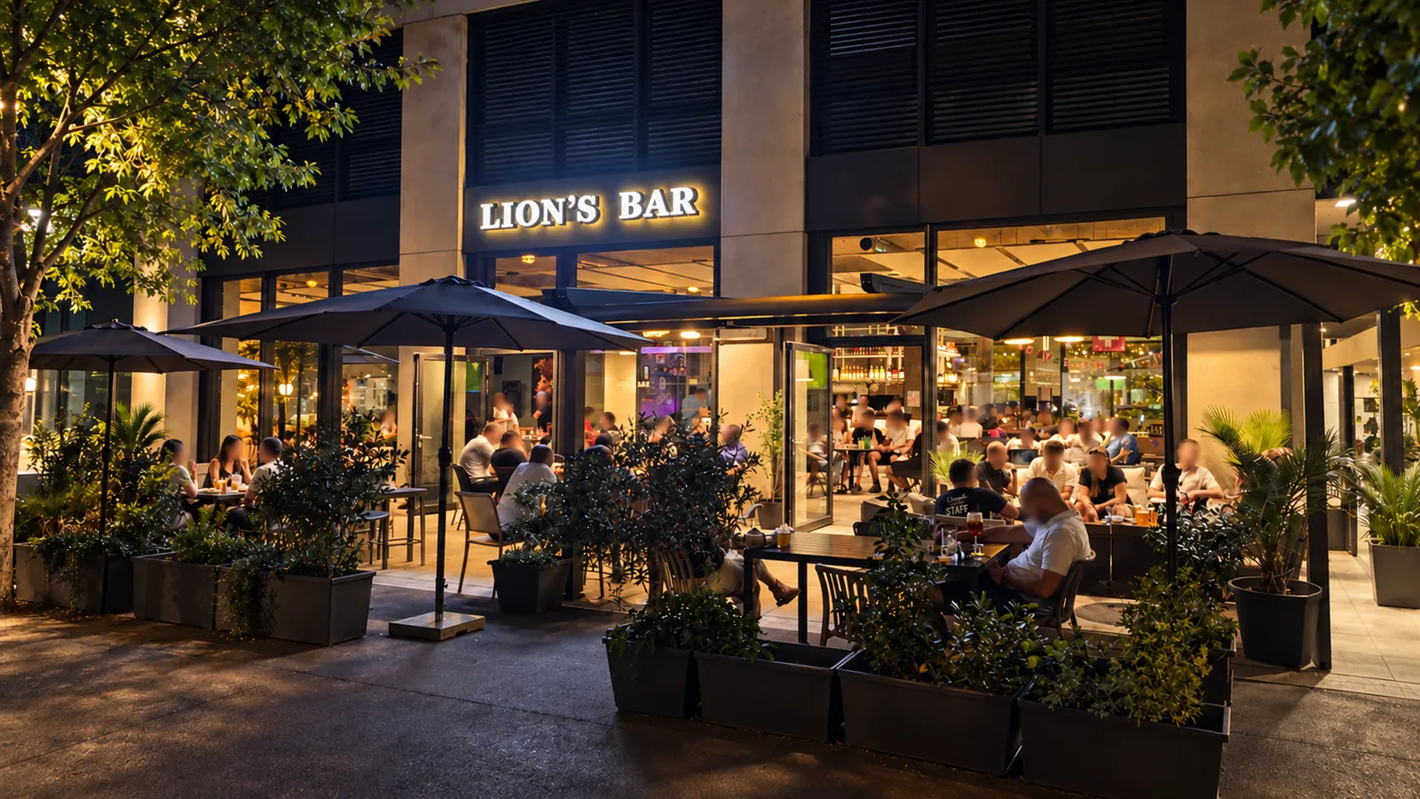 La façade du Lion’s Bar un soir, enseigne allumée et terrasse pleine